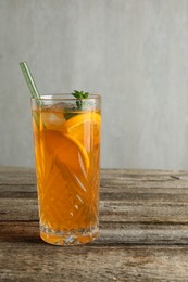 Photo of Glass of tasty refreshing drink and straw on wooden table against gray background