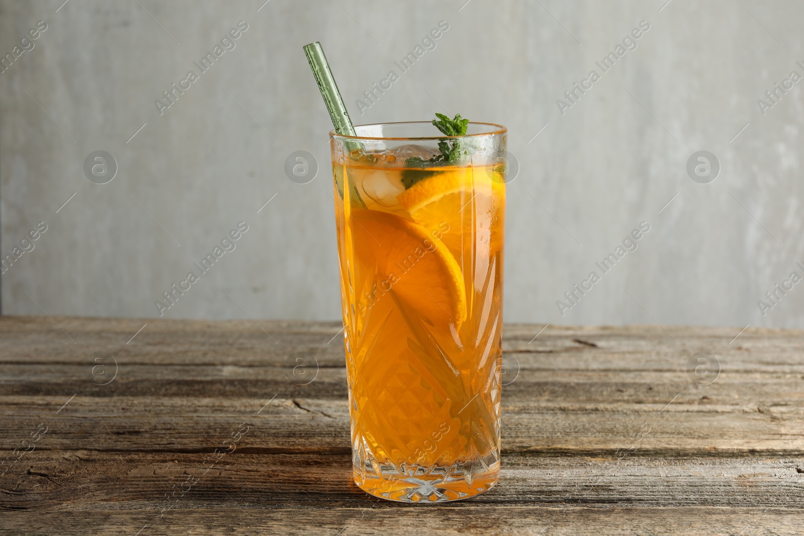 Photo of Glass of tasty refreshing drink and straw on wooden table against gray background