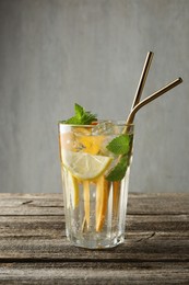 Glass of tasty refreshing drink and straws on wooden table against gray background