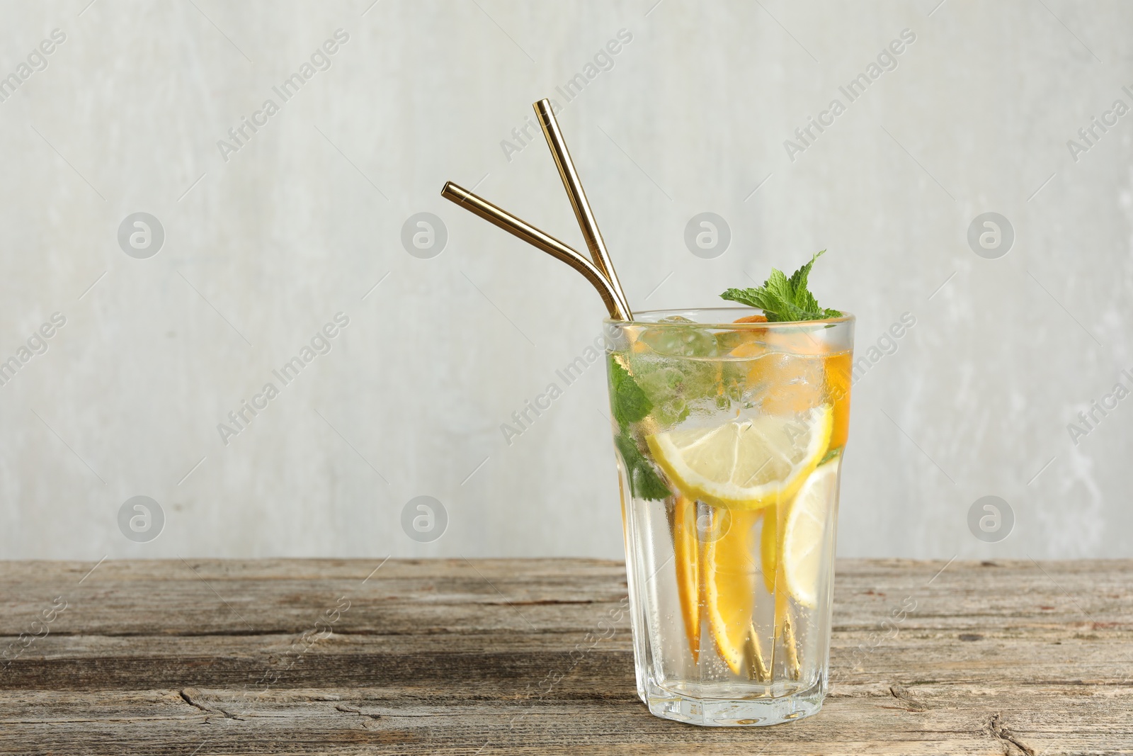 Photo of Glass of tasty refreshing drink and straws on wooden table against gray background, space for text