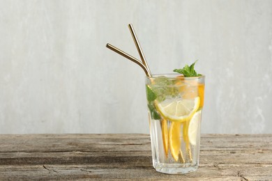 Photo of Glass of tasty refreshing drink and straws on wooden table against gray background, space for text