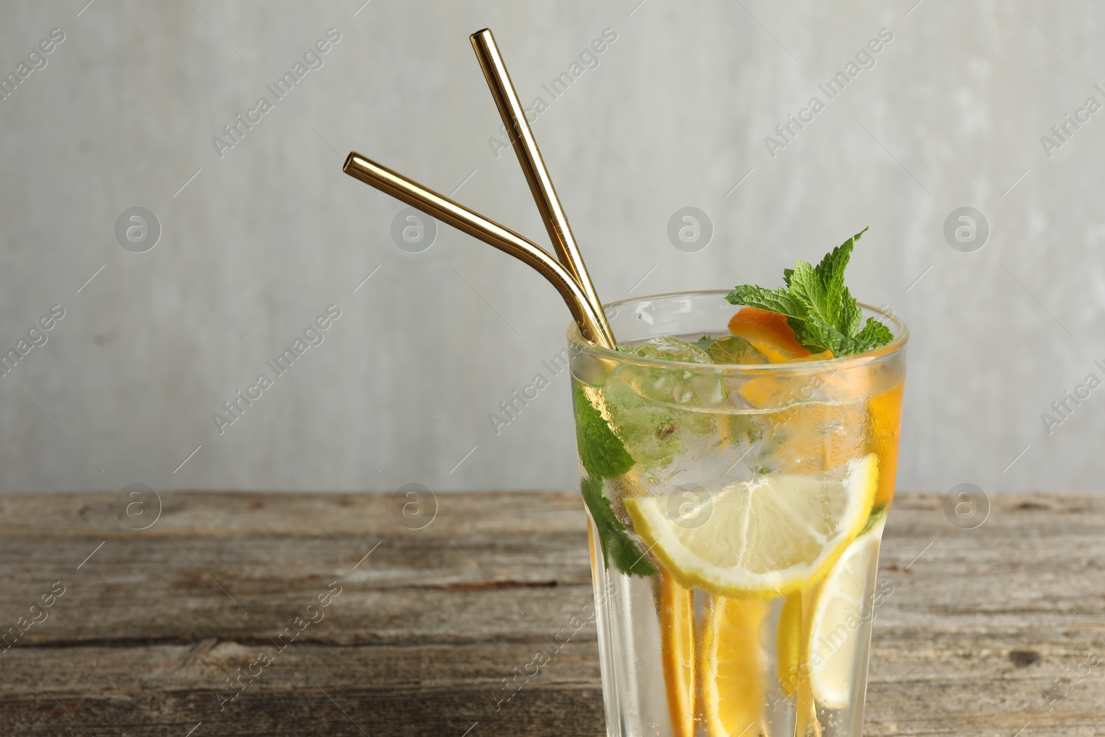 Photo of Glass of tasty refreshing drink and straws on wooden table against gray background, closeup