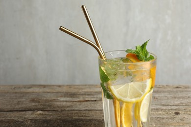 Glass of tasty refreshing drink and straws on wooden table against gray background, closeup