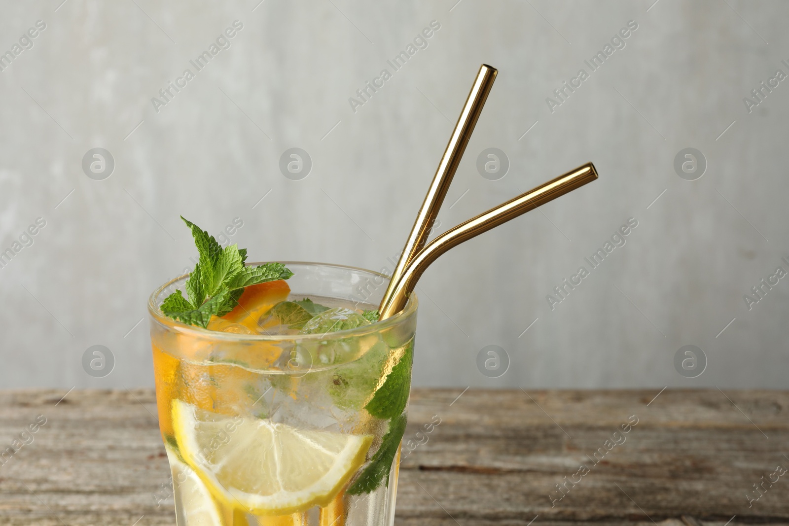 Photo of Glass of tasty refreshing drink and straws on wooden table against gray background, closeup