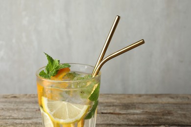 Photo of Glass of tasty refreshing drink and straws on wooden table against gray background, closeup