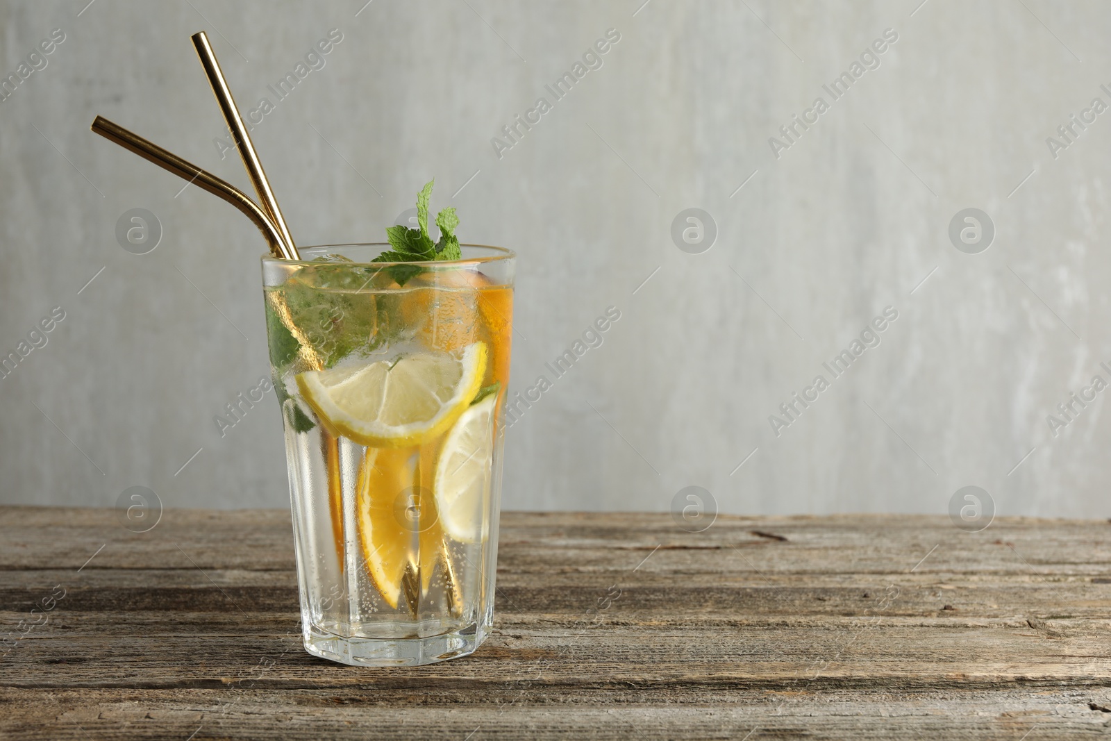 Photo of Glass of tasty refreshing drink and straws on wooden table against gray background, space for text