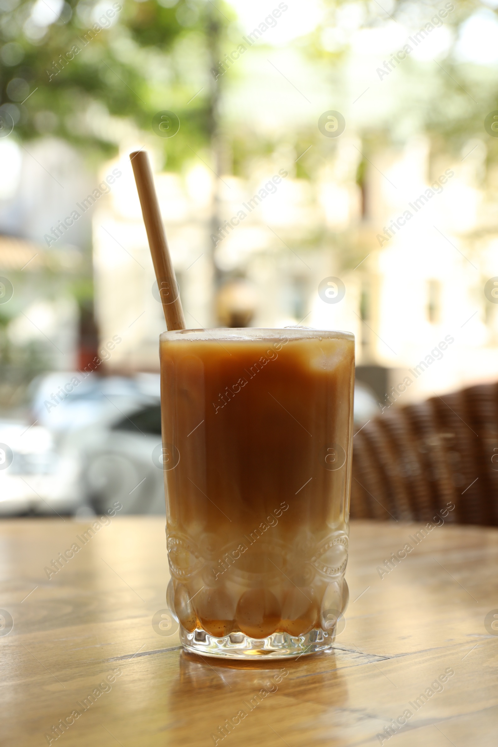 Photo of Glass of refreshing iced coffee and straw on wooden table outdoors