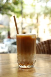 Photo of Glass of refreshing iced coffee and straw on wooden table outdoors