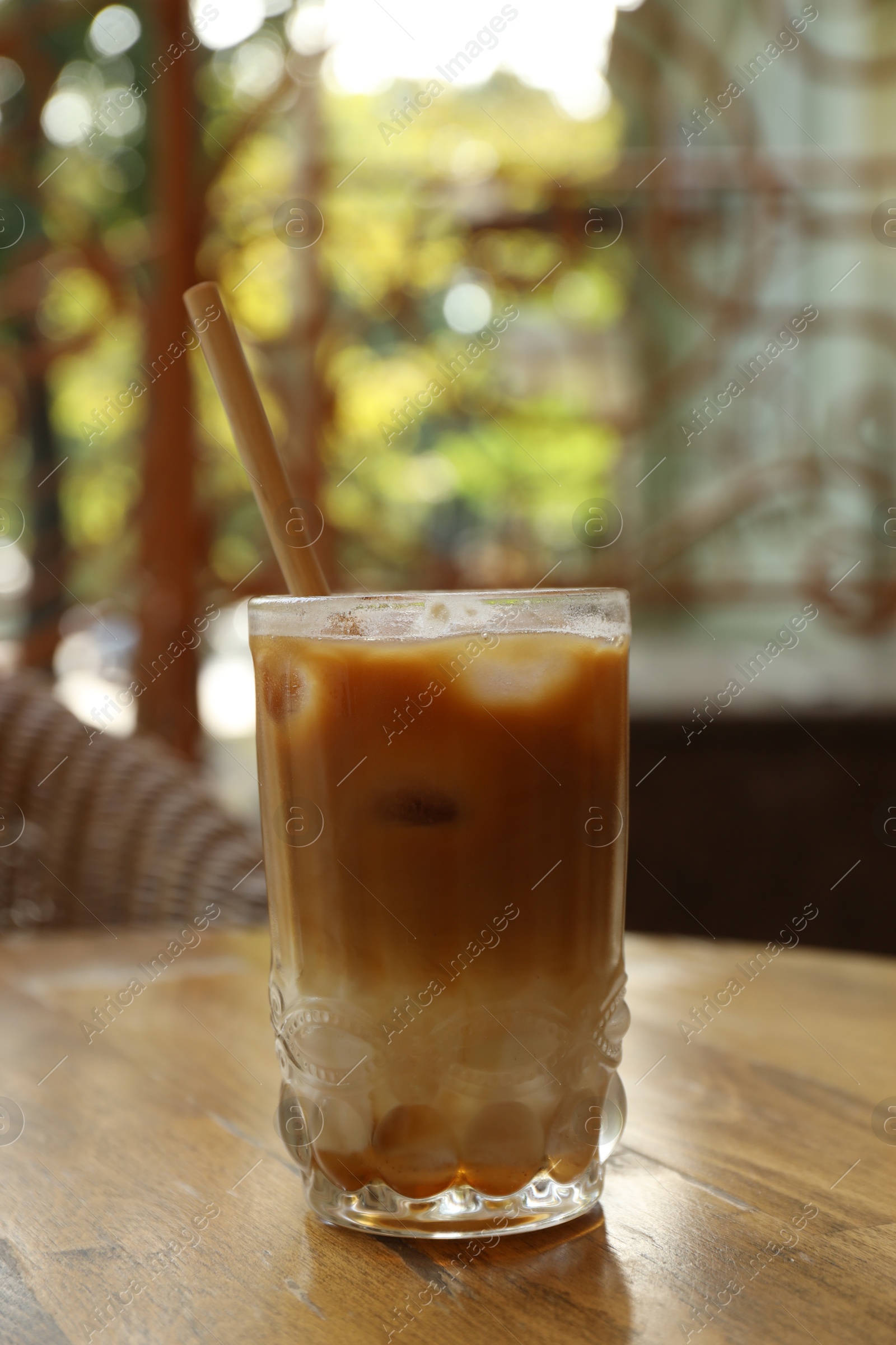 Photo of Glass of refreshing iced coffee and straw on wooden table outdoors