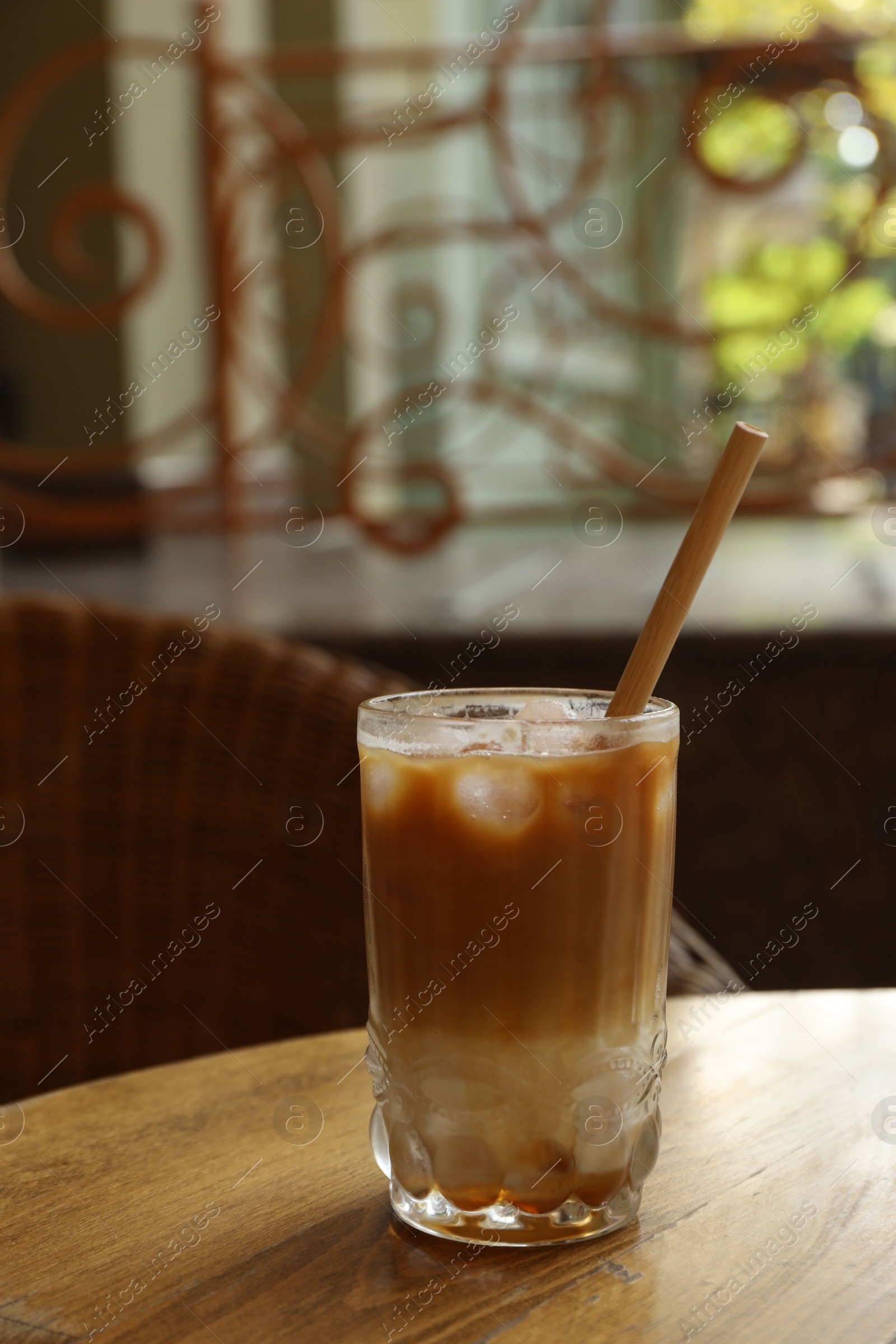 Photo of Glass of refreshing iced coffee and straw on wooden table outdoors