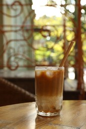 Glass of refreshing iced coffee and straw on wooden table outdoors