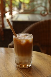 Photo of Glass of refreshing iced coffee and straw on wooden table outdoors