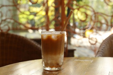 Photo of Glass of refreshing iced coffee and straw on wooden table outdoors