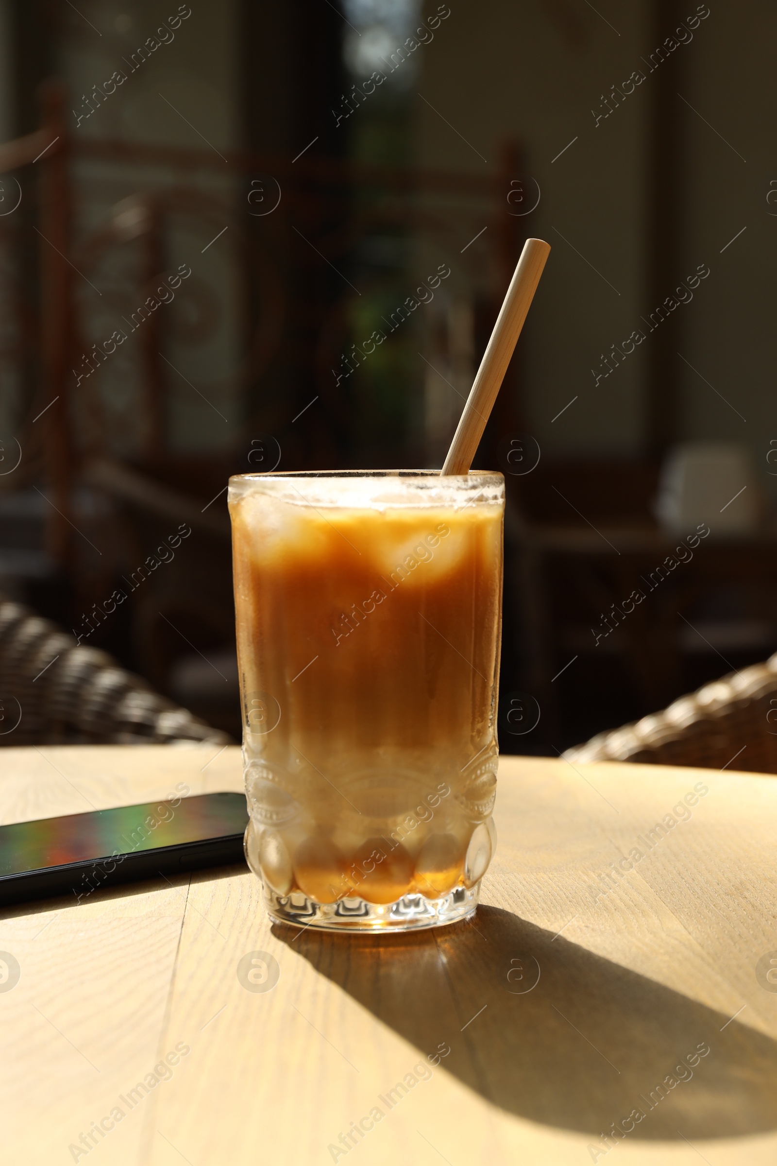 Photo of Glass of refreshing iced coffee and straw on wooden table outdoors