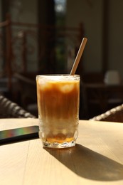 Photo of Glass of refreshing iced coffee and straw on wooden table outdoors