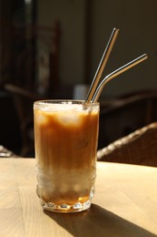 Photo of Glass of refreshing iced coffee and straws on wooden table outdoors