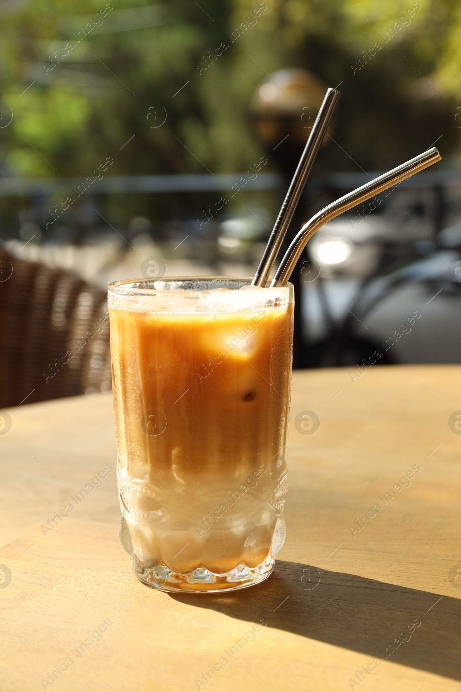 Photo of Glass of refreshing iced coffee and straws on wooden table outdoors