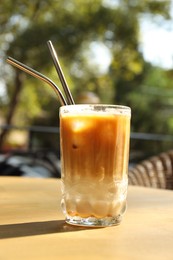 Glass of refreshing iced coffee and straws on wooden table outdoors