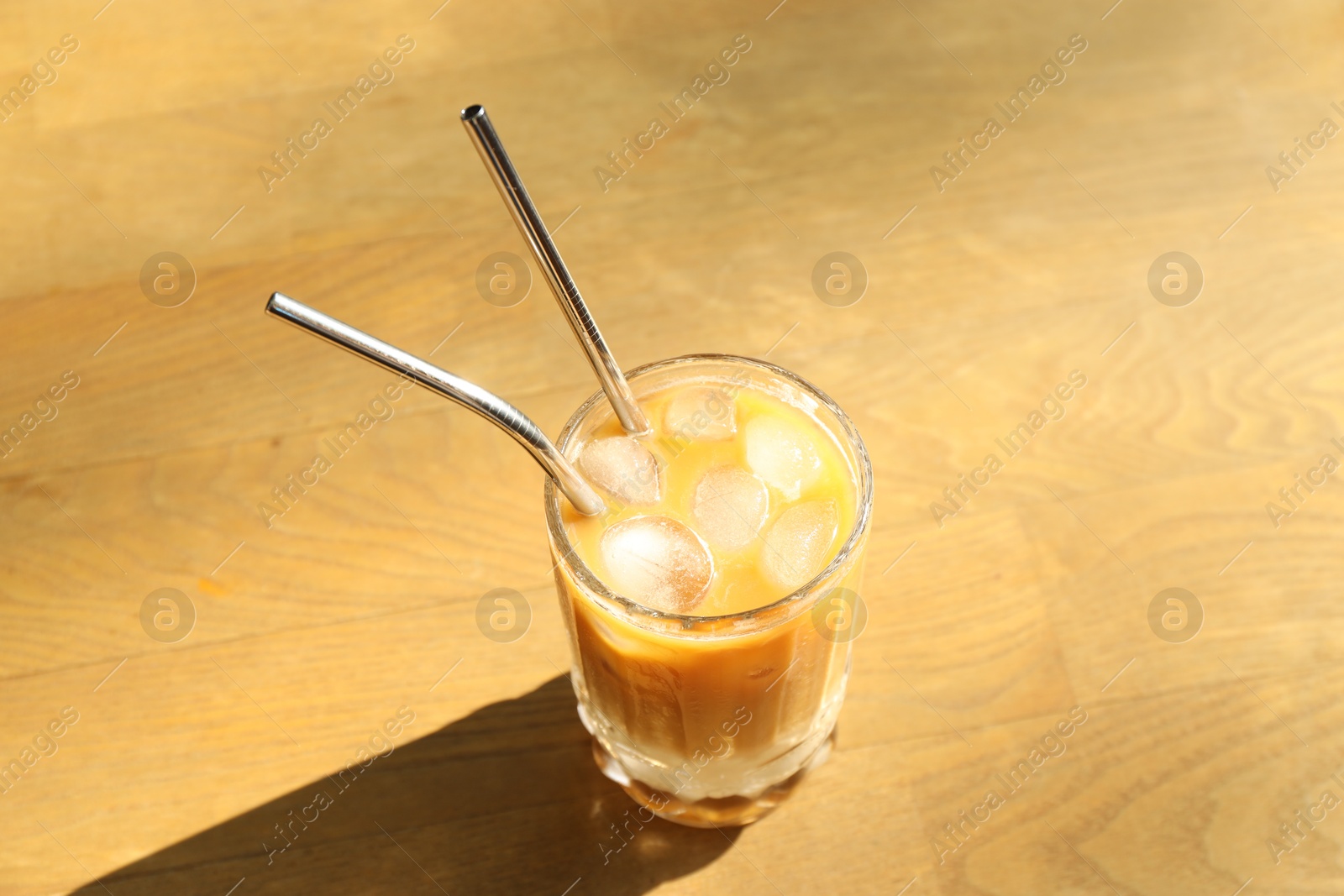 Photo of Glass of refreshing iced coffee and straws on wooden table outdoors, above view