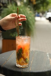 Photo of Woman taking straw from glass with tasty refreshing drink on wooden table outdoors, closeup