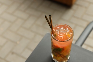 Glass of tasty refreshing drink and straws on table outdoors, space for text