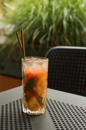 Glass of tasty refreshing drink and straws on table in outdoor cafe