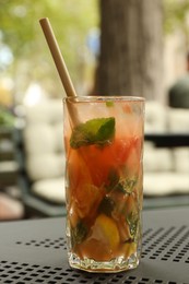 Photo of Glass of tasty refreshing drink and straw on table in outdoor cafe