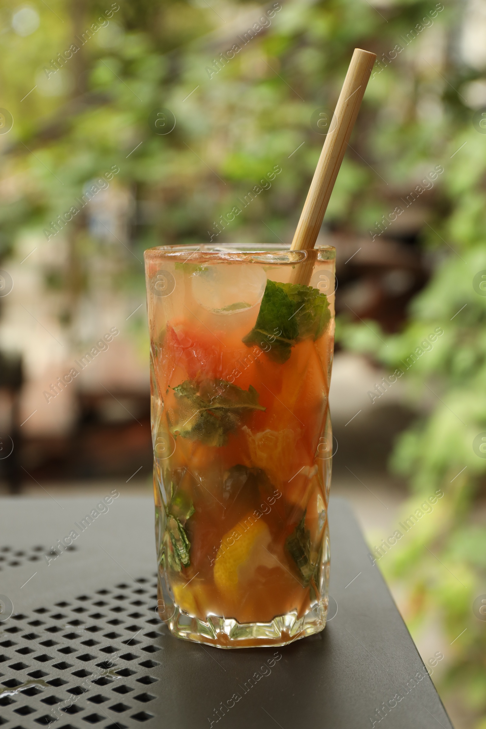 Photo of Glass of tasty refreshing drink and straw on table in outdoor cafe