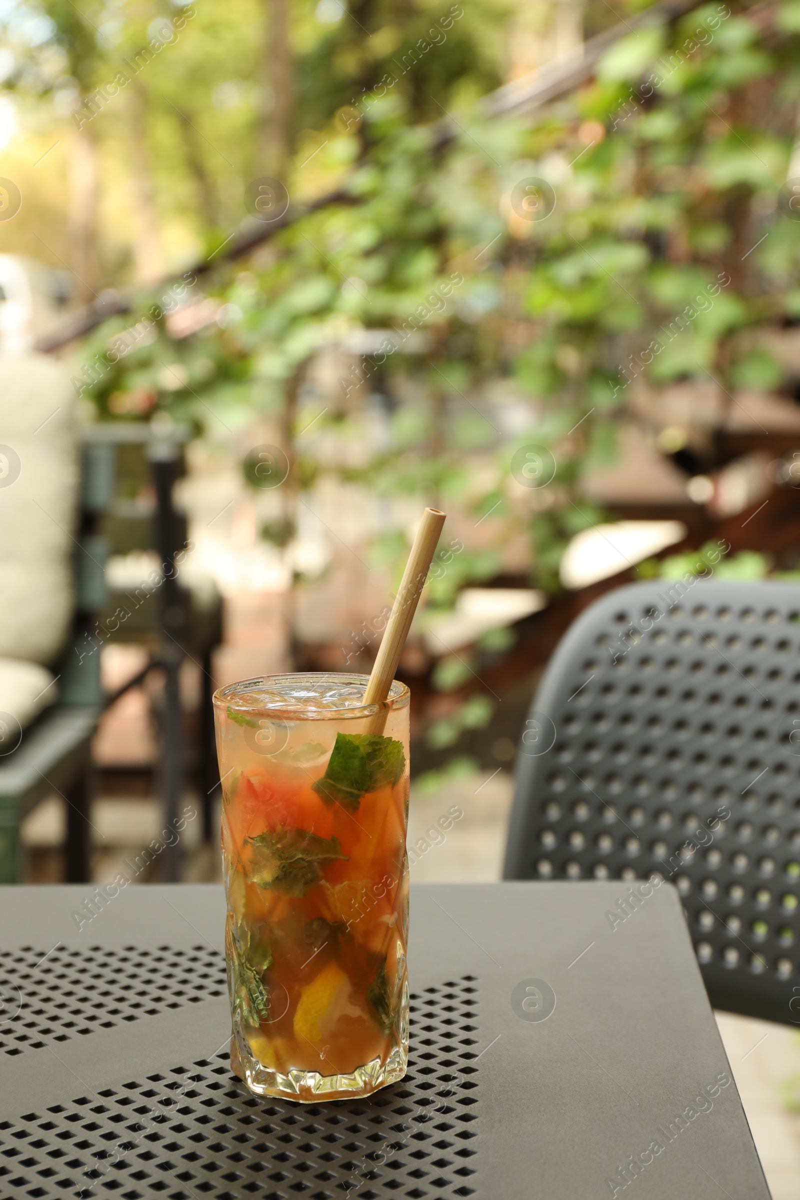 Photo of Glass of tasty refreshing drink and straw on table in outdoor cafe