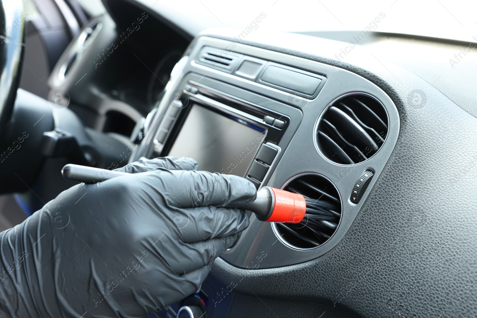 Photo of Man cleaning air vent with brush in car, closeup