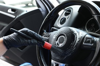 Man cleaning steering wheel with brush in car, closeup