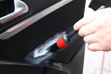 Photo of Man cleaning car door with brush, closeup