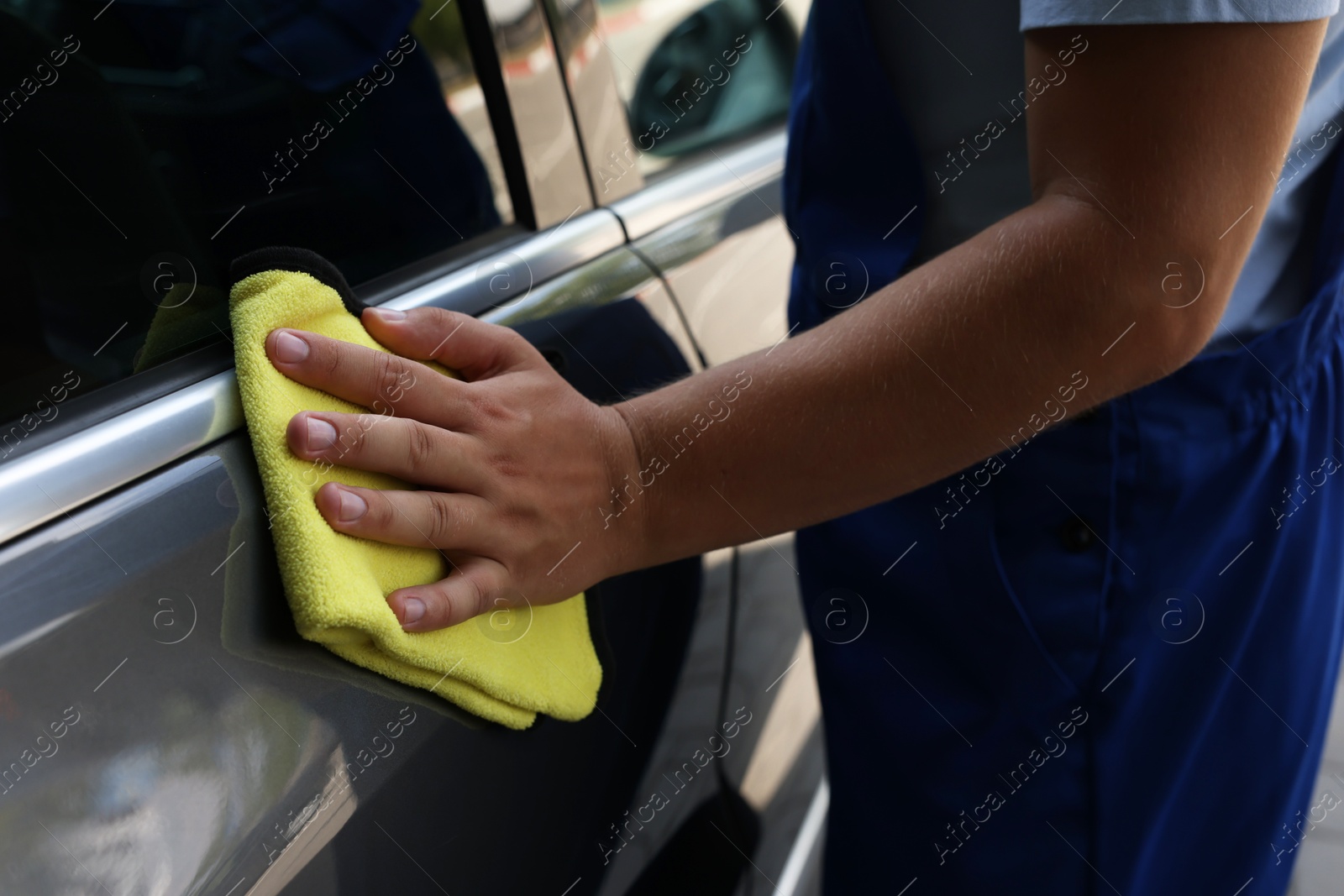 Photo of Man wiping car door with yellow rag, closeup