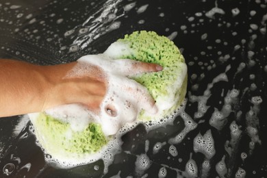 Photo of Man washing car hood with sponge indoors, closeup