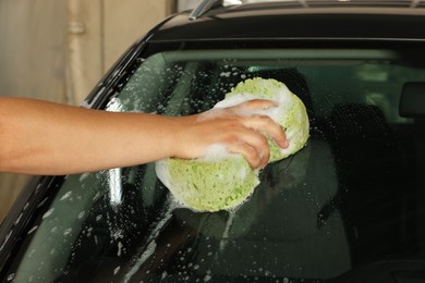 Photo of Man washing car windshield with sponge indoors, closeup