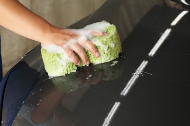 Photo of Man washing car hood with sponge indoors, closeup