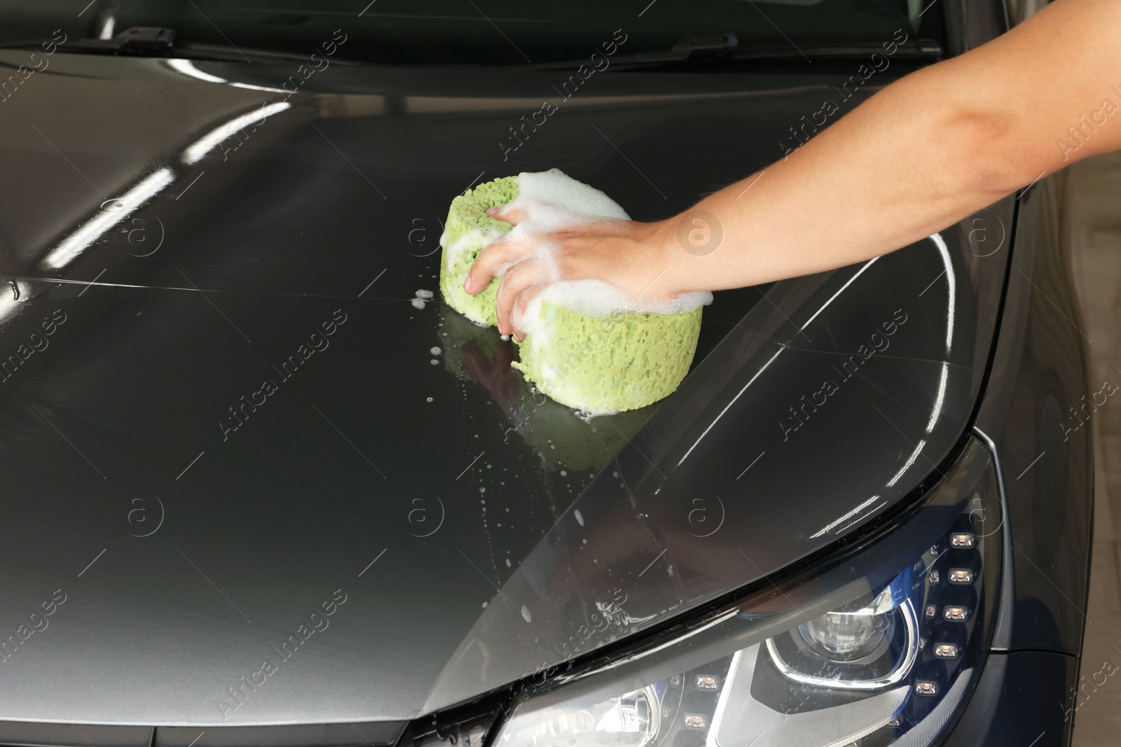 Photo of Man washing car hood with sponge indoors, closeup