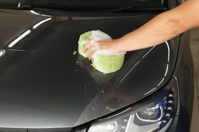 Man washing car hood with sponge indoors, closeup