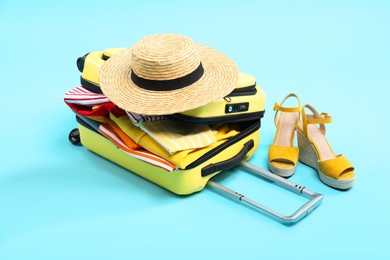 Photo of Yellow suitcase with clothes, shoes and wicker hat on light blue background