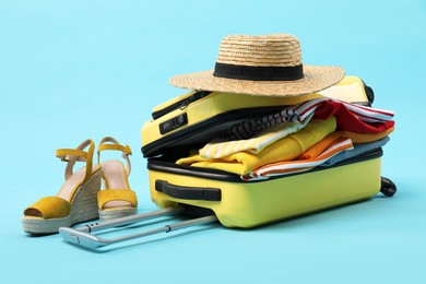 Photo of Yellow suitcase with clothes, shoes and wicker hat on light blue background