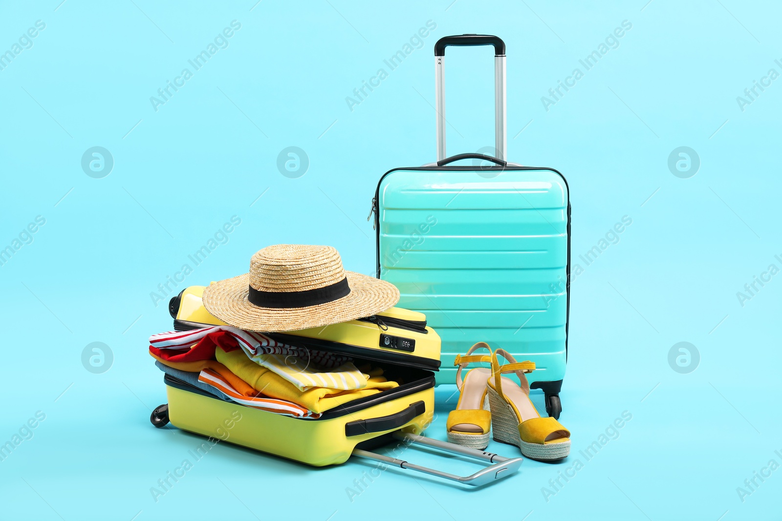 Photo of Suitcases with clothes, shoes and wicker hat on light blue background