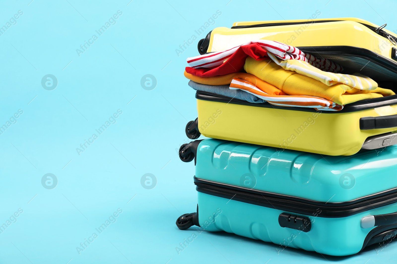 Photo of Two suitcases with clothes on light blue background, space for text