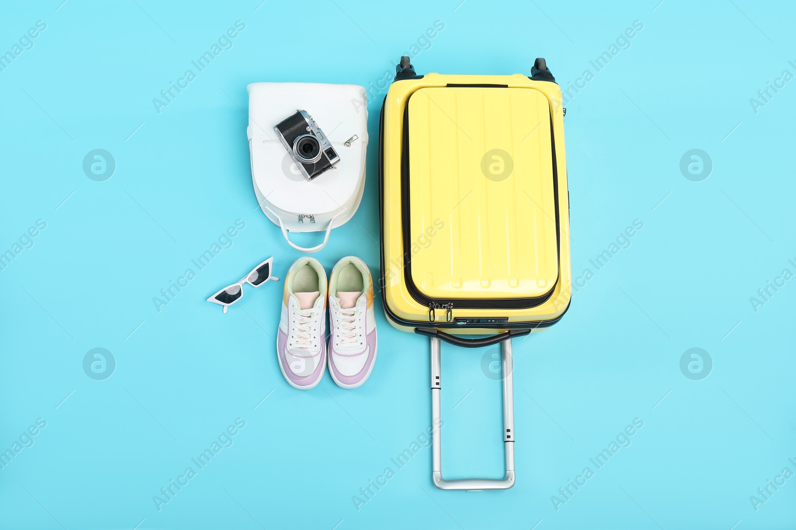 Photo of Yellow suitcase, sneakers, sunglasses, backpack and camera on light blue background, flat lay