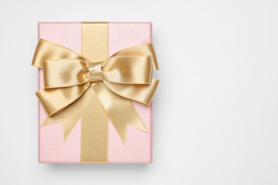 Photo of Gift box with golden bow on light grey background, top view. Space for text