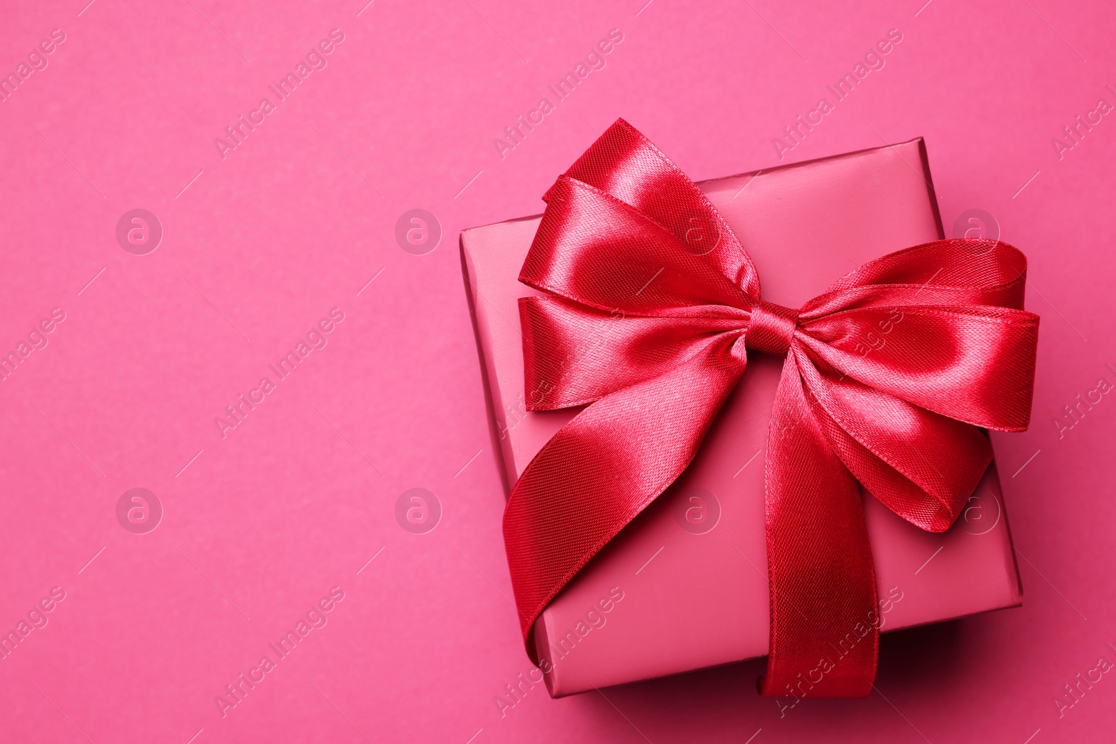 Photo of Gift box with bow on pink background, top view. Space for text