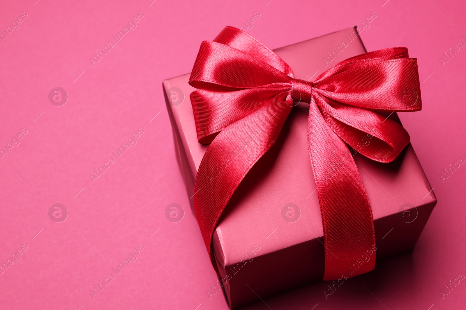 Photo of Gift box with bow on pink background. Space for text