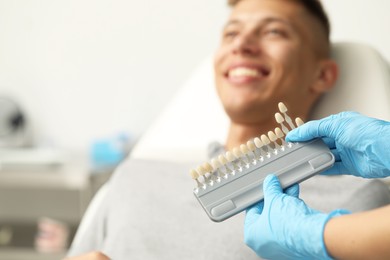 Doctor checking young man's teeth color in clinic, selective focus. Dental veneers