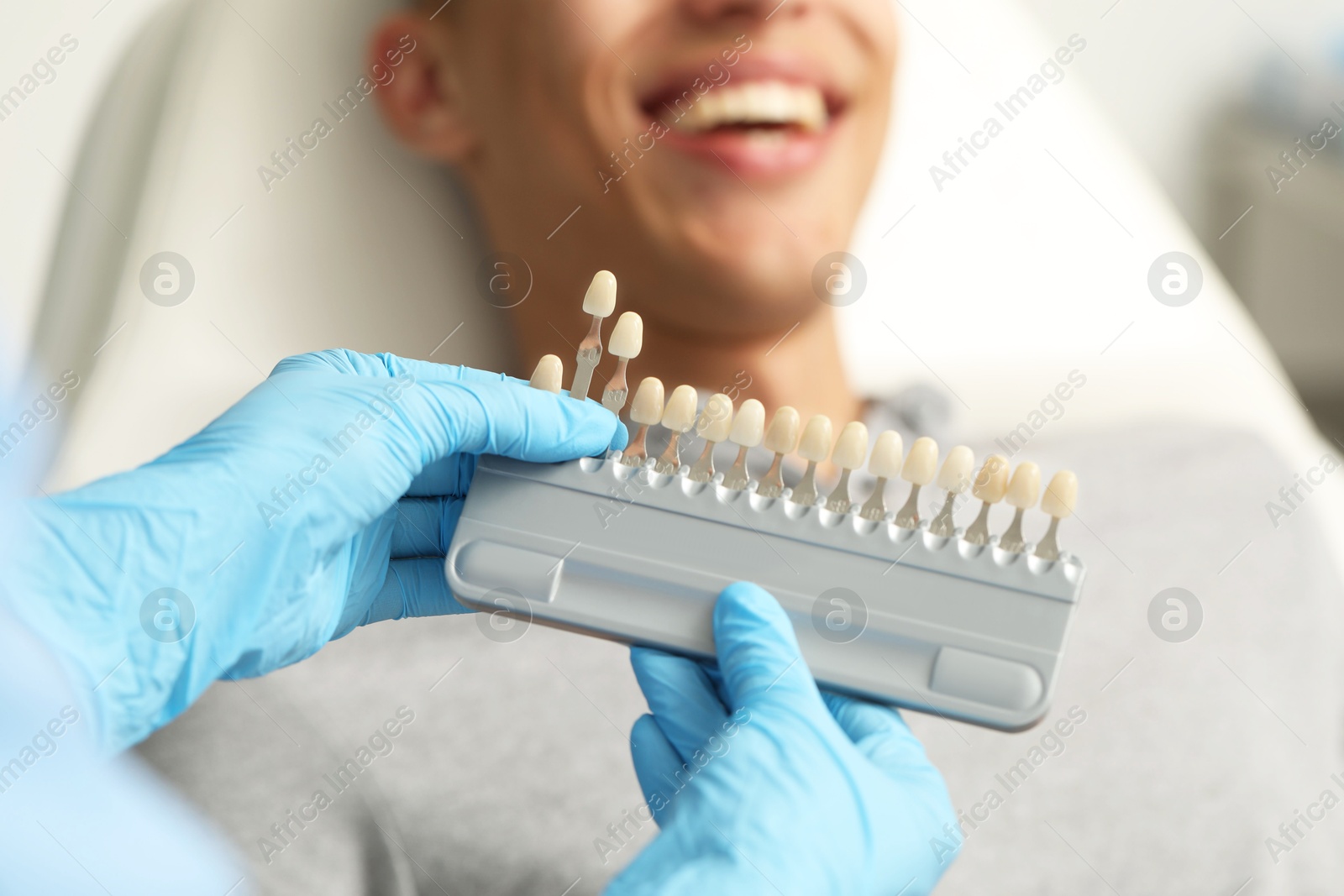 Photo of Doctor checking young man's teeth color in clinic, closeup. Dental veneers