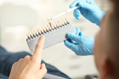 Doctor and patient choosing shade on teeth color palette in clinic, closeup. Dental veneers