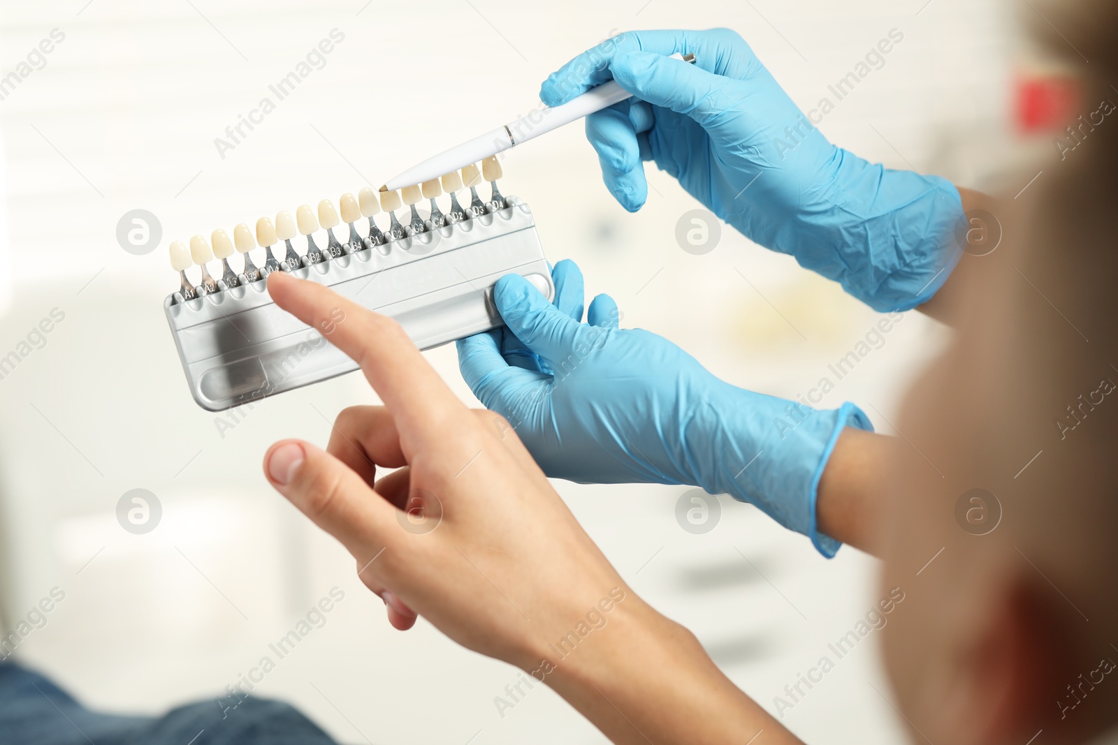 Photo of Doctor and patient choosing shade on teeth color palette in clinic, closeup. Dental veneers